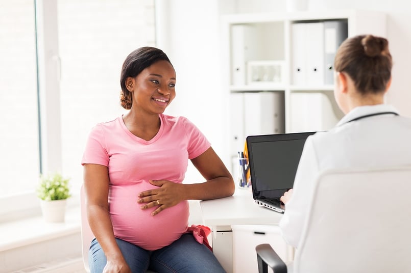 A photo of a young, pregnant woman visiting her doctor for a regular checkup.