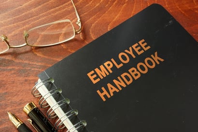 A photo of a spiral bound employee handbook lying on a wood desk.