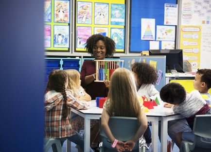 A photo of a teacher sitting at a small table with a group of students.