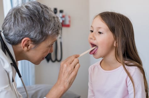 A photo of a doctor using a tongue depressor to look at a child's throat. 
