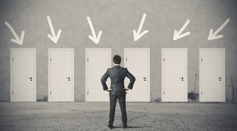 A photo of a man standing in front of six doors, trying to decide which to choose.