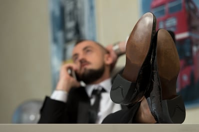 A photo of a business man leaning back in a chair with his feet on the desk. time to fire your benefits broker?