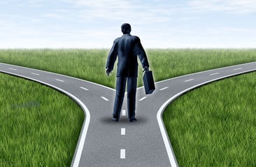 A cartoon image of a man standing at a fork in the road, trying to decide which direction to go.