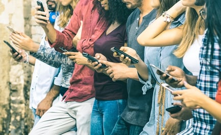 A photo of eight young people in a line, all looking at their smartphones.