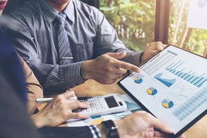 A photo of someone pointing to level funded planning charts and graphs on a tablet during a meeting.