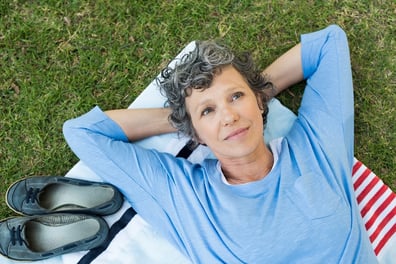 A photo of a retired person lying on a blanket in the grass, looking up to the sky.