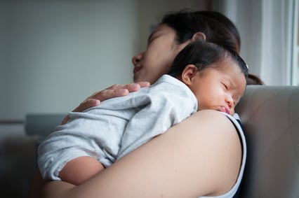 A photo of a baby sleeping on his mother's shoulder.