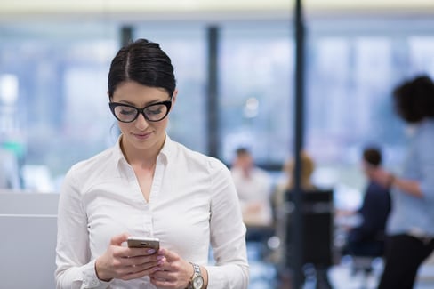 A photo of a woman walking through an office, looking down at her smartphone.