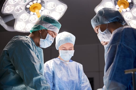 A photo of four surgeons in an operating room with lights shining bright over their heads.
