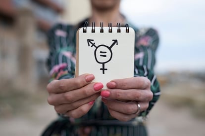 A photo of someone holding up a small notepad with a transgender symbol drawn on it.