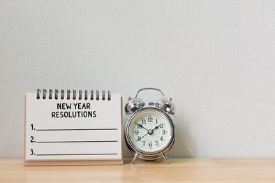 A photo of an alarm clock on a desk with a notepad to write new year's resolutions.