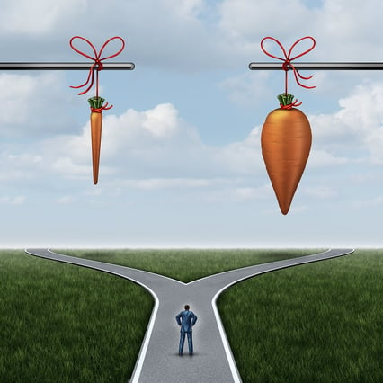cartoon man standing at a fork in the road beneath a skinny carrot and a fat carrot. 