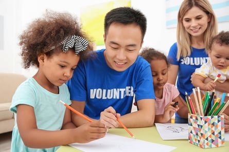 A photo of two people volunteering with small kids in a classroom.