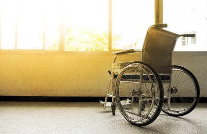 A photo of an empty wheelchair sitting next to window with the sun shining brightly through it.