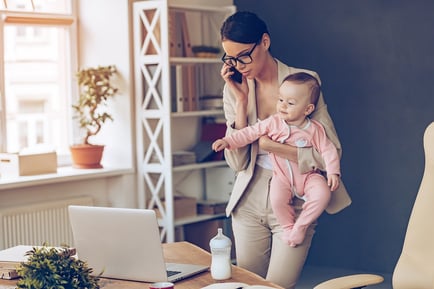 A photo of a woman holding her baby while on a work call in her office.